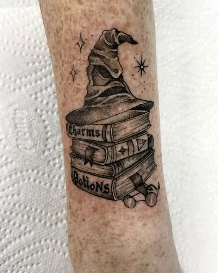 Black and grey sorting hat on a stack of books with lettered spines, on a forearm