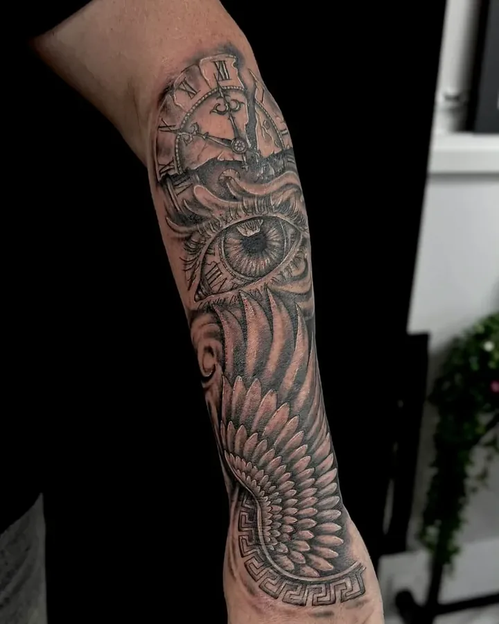 Black and grey winged eye with a clock, on a forearm